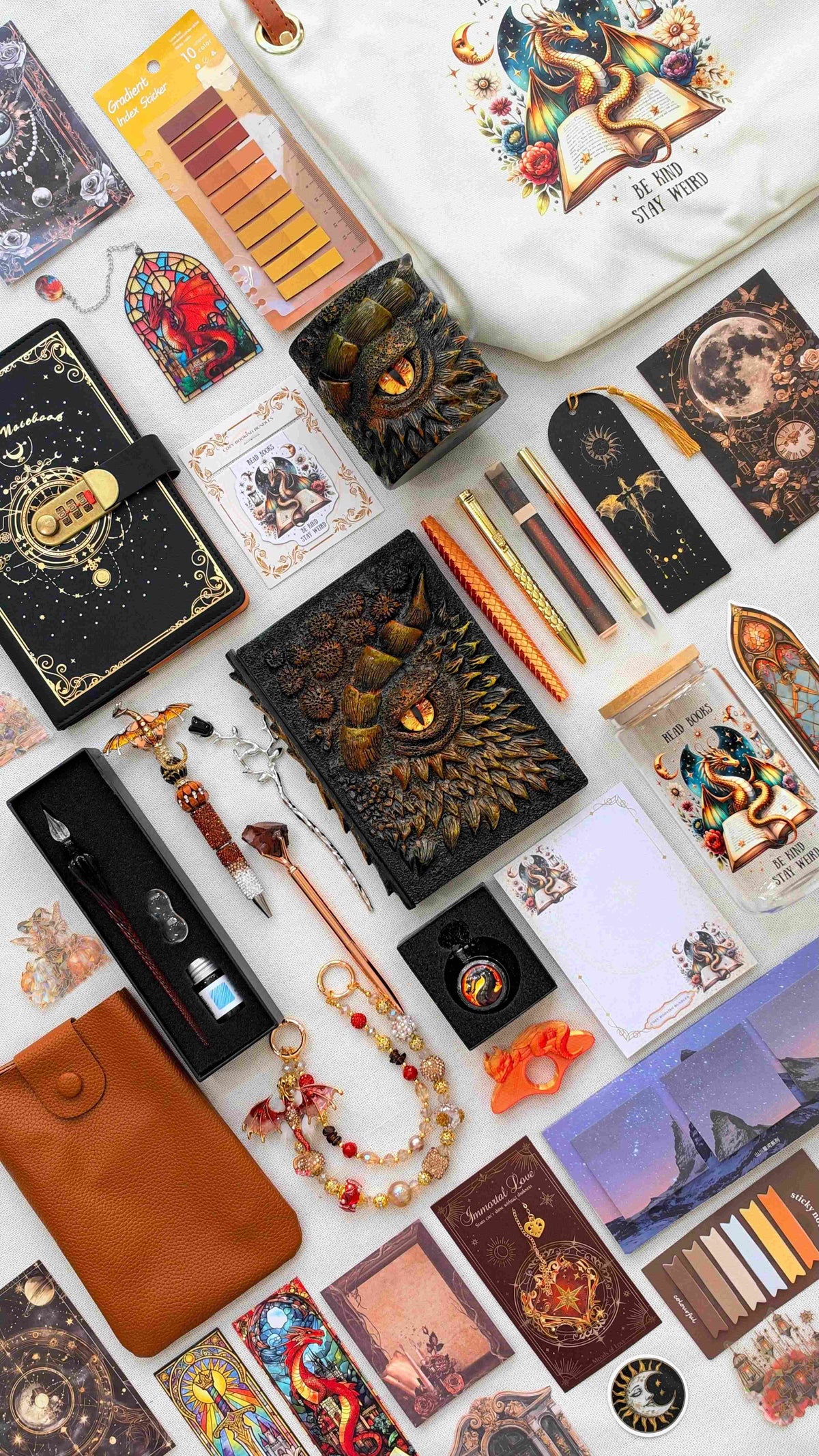 Gilded Ember Velvet Edition black and gold dragon bookish bundle with a sculpted dragon eye notebook and matching pen holder organizer. Orange and gold pens, a glass dip pen set, fantasy bookmarks, sticky notes and reading tabs are displayed with an extra notebook, dragon print tote bag and glass jar, orange crossbody bag, dragon charm and pocket watch.