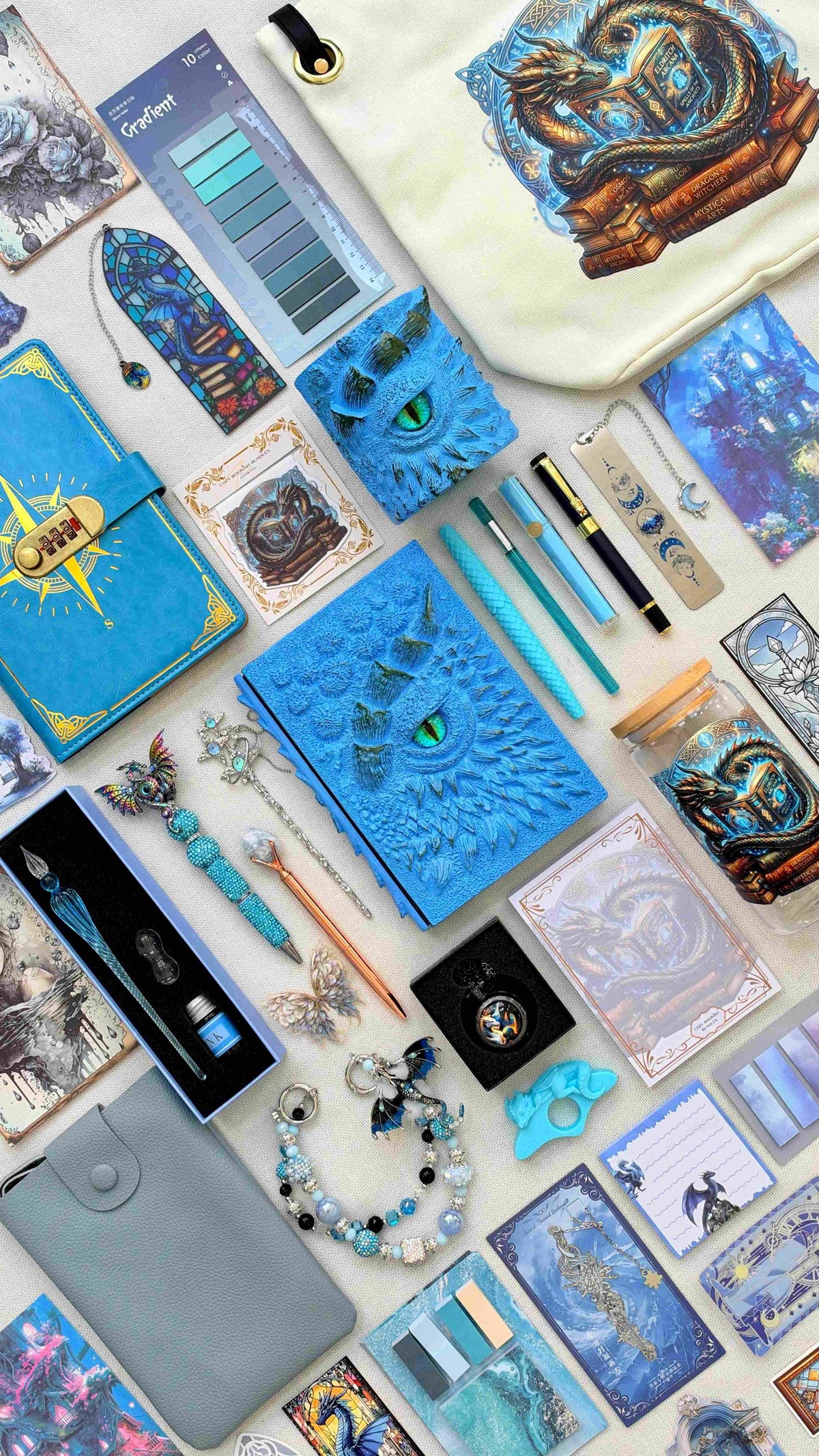 Ice Crystal Velvet Edition blue dragon bookish bundle with a sculpted dragon eye notebook and matching pen holder organizer, pens, glass dip pen set, fantasy bookmarks, sticky notes and reading tabs. Includes an extra notebook, dragon print tote bag and glass jar, pale blue crossbody bag, dragon charm and pocket watch.