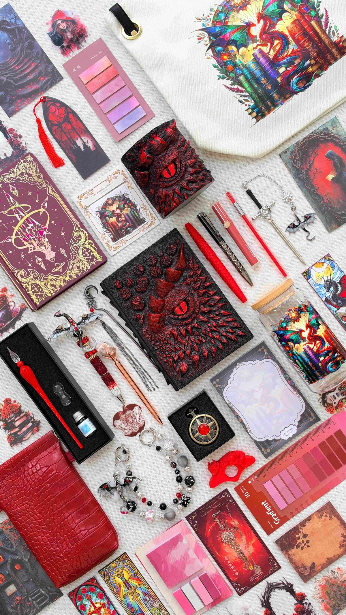 Inferno Eye Velvet Edition black and red dragon bookish bundle with a sculpted dragon eye notebook and matching pen holder organizer, red pens, glass dip pen set, fantasy bookmarks, sticky notes and reading tabs. Arranged with an extra notebook, dragon print tote bag and glass jar, red crossbody bag, dragon charm and pocket watch.