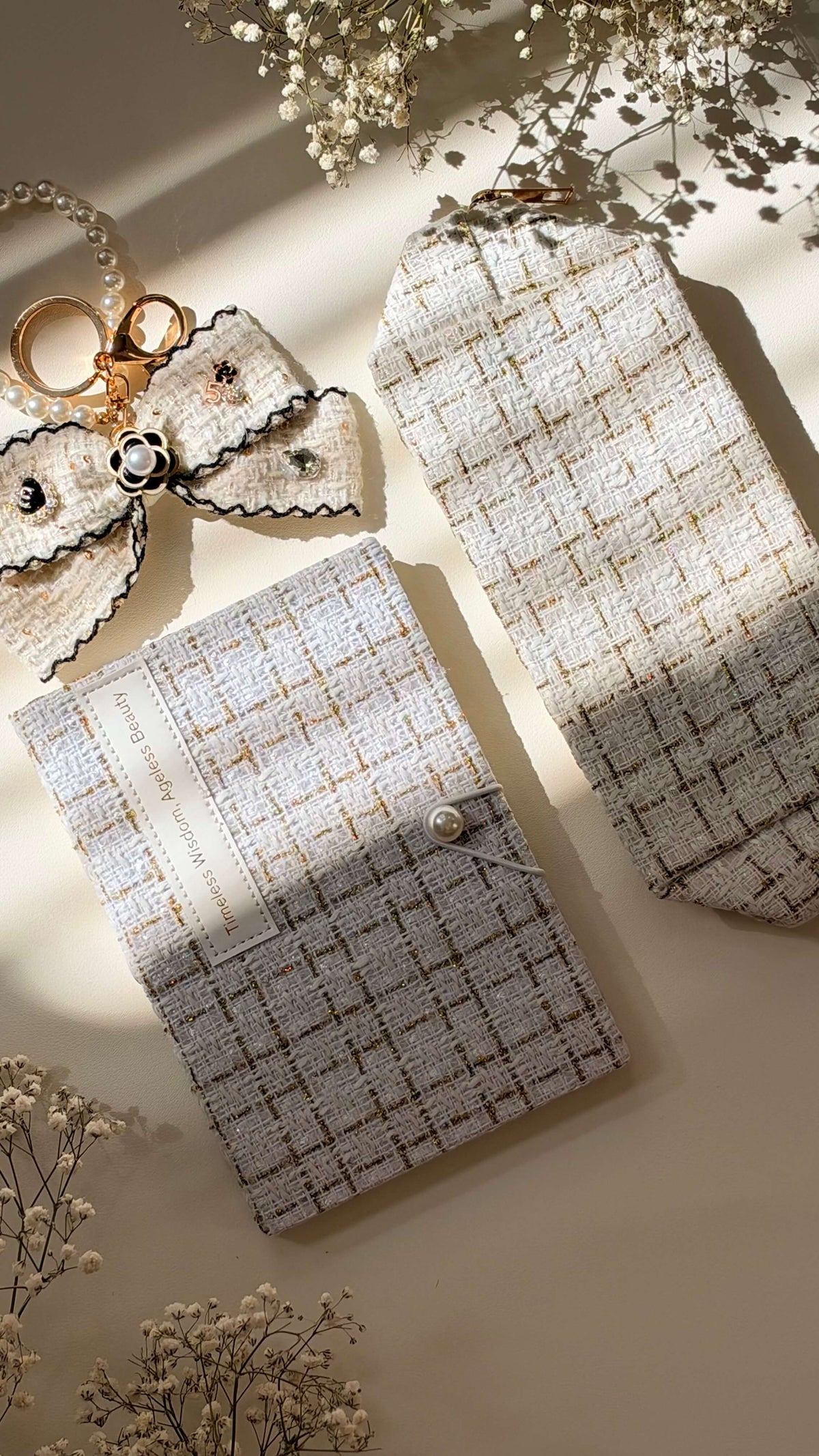 Close-up of the Ivory Linen Edition in pale tweed, showing matching pouches, a lace bow with pearl details, and a gold keychain on a warm beige surface.
