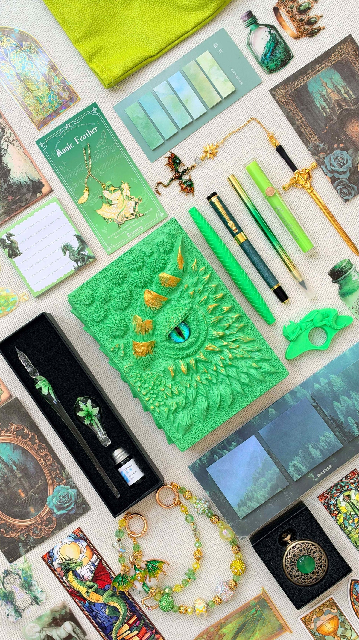 Mystic Sage Linen Edition green dragon bookish bundle with a sculpted dragon eye notebook with gold horns, green pens and highlighter, glass dip pen and ink set, fantasy bookmarks, sticky notes, pastel page tabs, dragon thumb page holder, beaded dragon charm, pocket watch and bright green crossbody bag.