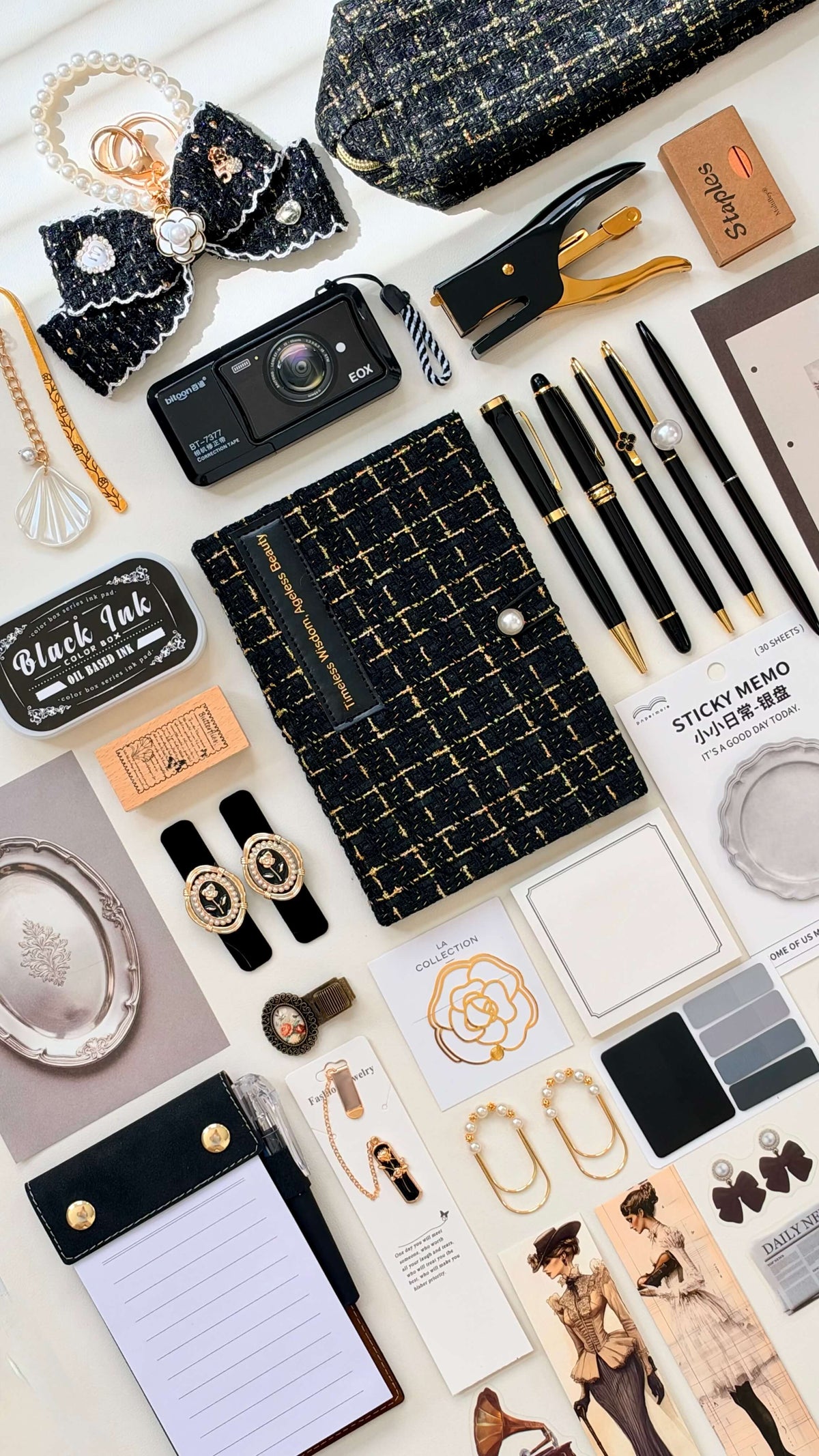 Noir Velvet Edition bookish bundle in a black-and-gold flat lay with a patterned notebook, pens, camera, jewelry, and small accessories.