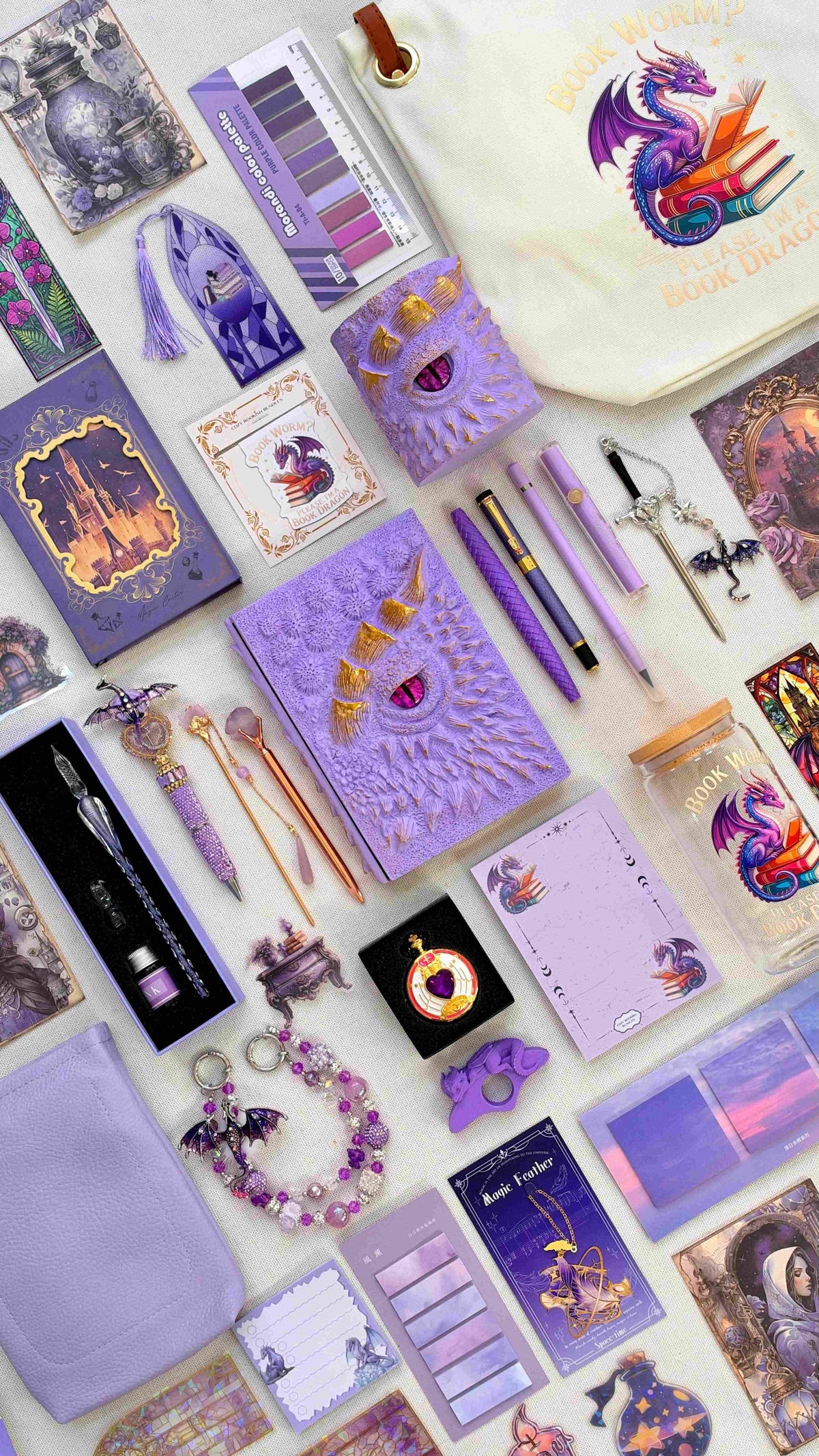Soft Purple Velvet Edition lilac dragon bookish bundle with a sculpted dragon eye notebook and matching pen holder organizer. Purple pens, a glass dip pen and ink set, fantasy bookmarks, sticky notes, reading tabs, pocket watch, dragon charm and extra notebook are displayed with a lavender crossbody bag, dragon print glass jar and dragon and books tote bag.