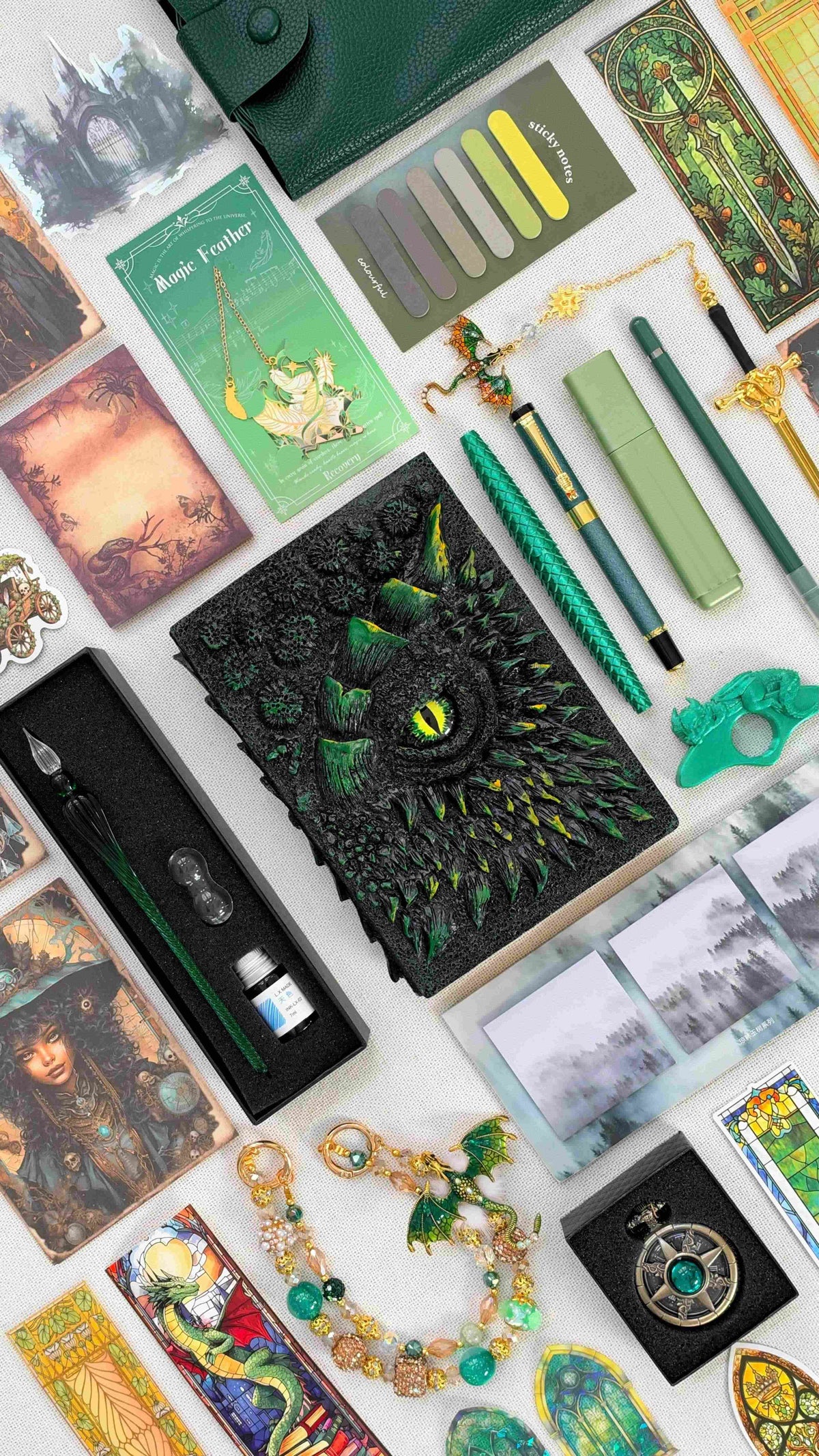 Venom Emerald Linen Edition black and green dragon bookish bundle with a sculpted dragon eye notebook, green dragon scale pen, glass dip pen and ink set, highlighter, fantasy bookmarks, sticky notes, page tabs, dragon thumb page holder, beaded dragon charm, pocket watch and dark green crossbody bag.