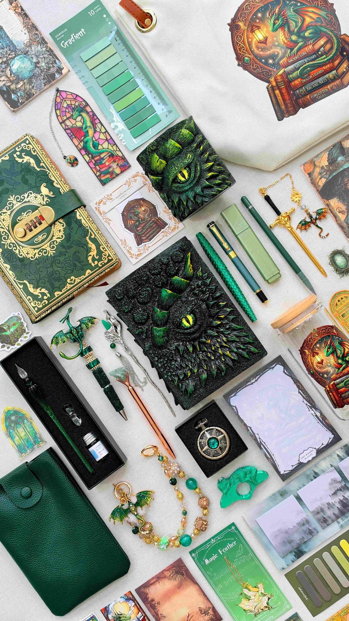 Venom Emerald Velvet Edition black and green dragon bookish bundle with a sculpted dragon eye notebook and matching pen holder organizer, green pens, glass dip pen set, fantasy bookmarks, sticky notes and reading tabs. Includes an extra notebook, dragon print tote bag and glass jar, dark green crossbody bag, dragon charm and pocket watch.